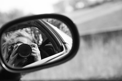 Reflection of woman photographing on side-view mirror