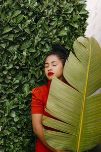 Woman holding green banana leaf while standing in front of plants