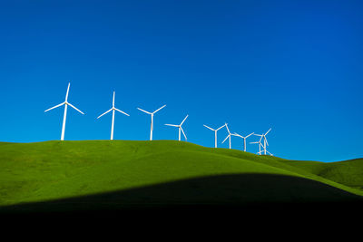 Windmills on field against blue sky