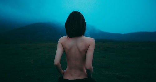 Rear view of shirtless woman on grass against mountain and sky during foggy weather