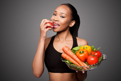 Portrait of young woman holding red bell pepper against black background