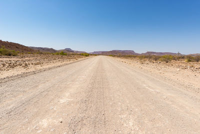 Dirt road amidst land against clear sky