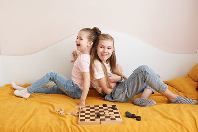 Sisters playing draughts board game on bed