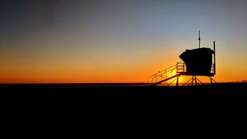 Silhouette water tower on land against sky during sunset