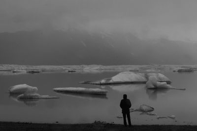 Rear view of man standing in lake against sky