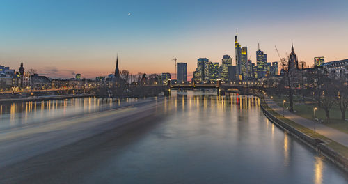 View of river against illuminated buildings during sunset