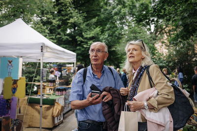 Confused senior man and woman looking away while standing at market place