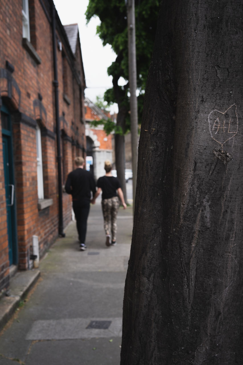 REAR VIEW OF PEOPLE WALKING ON FOOTPATH AMIDST STREET