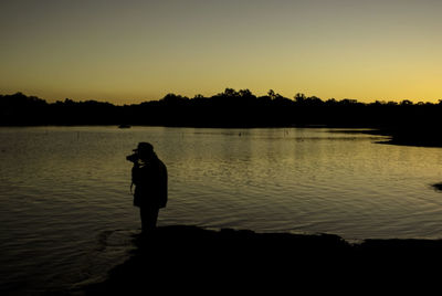 Silhouette man on lake against sky during sunset