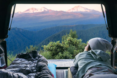 Young woman laying in back of truck looking out at mountains