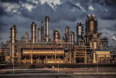 Metal storage containers with pipes in factory against cloudy sky