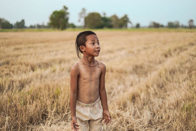 Thoughtful boy looking away while standing on field at farm