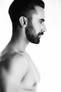 Side view of shirtless young man looking away while standing against white background