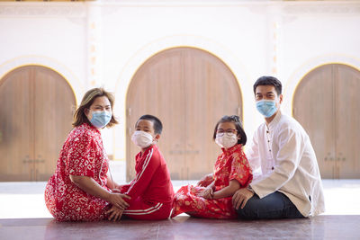 Asian family wearing red chinese suit wearing protection mask sitting outdoor
