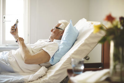 Senior man taking selfie with smart phone on bed in hospital ward