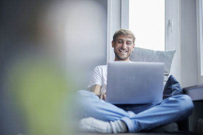 Smiling businessman using laptop sitting on sofa at home