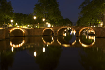 Illuminated bridge over river in city against sky at night