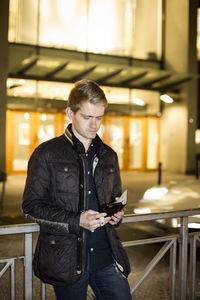 Young man using mobile phone while standing by railing