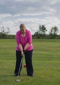 Full length of young woman playing with golf ball on field