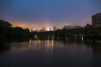 River by illuminated city against sky at sunset