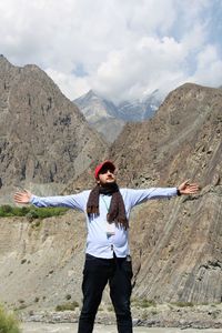 Young man with arms outstretched standing against mountains