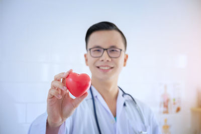 Portrait of smiling male doctor holding heart shape stress ball at hospital