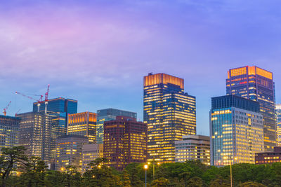 Illuminated buildings in city against sky at dusk