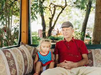Portrait of grandfather with cute granddaughter sitting on sofa