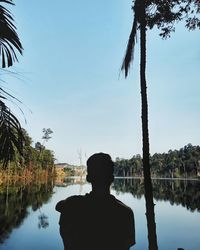 Rear view of man looking at lake against sky