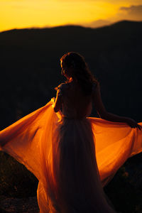 Woman looking away while standing on land against sky during sunset