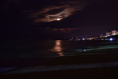 Illuminated city by sea against sky at night