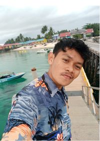 Portrait of man standing at harbor against cloudy sky