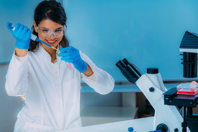 Student in white coat, working in research laboratory using micro pipette and test tube