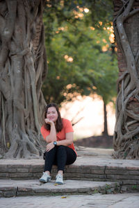 Portrait of a young woman sitting on tree trunk