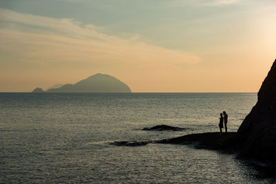 Silhouette people standing on beach against sky during sunset