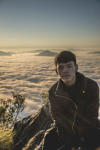 Portrait of young man standing on rock against sky