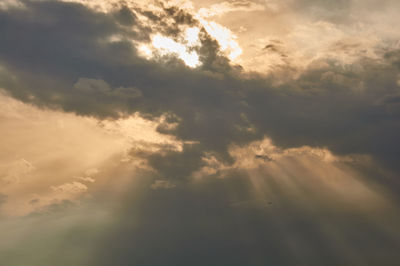 Low angle view of sunlight streaming through clouds