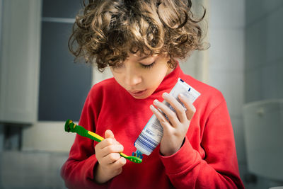 Cute boy applying paste on toothbrush standing in bathroom at home