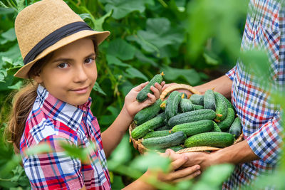 Portrait of smiling girl holding cucumbers at farm with father
