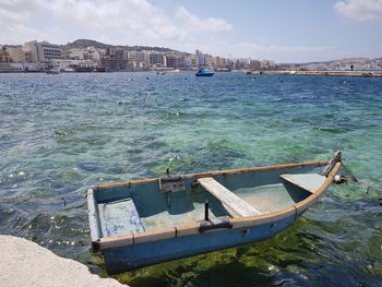 Boat moored on sea by city against sky