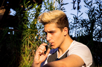 Portrait of young man looking away against trees