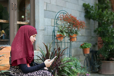 Woman in hjiab using mobile phone while sitting in back yard