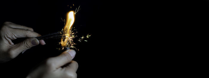 Close-up of hand holding sparkler against black background