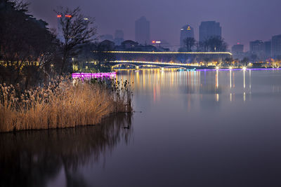 Illuminated city by river against sky at night