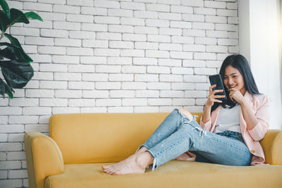 Young woman using mobile phone while sitting on wall