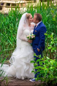 Wedding couple kissing while standing against plants