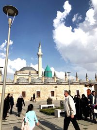 People in front of building against cloudy sky