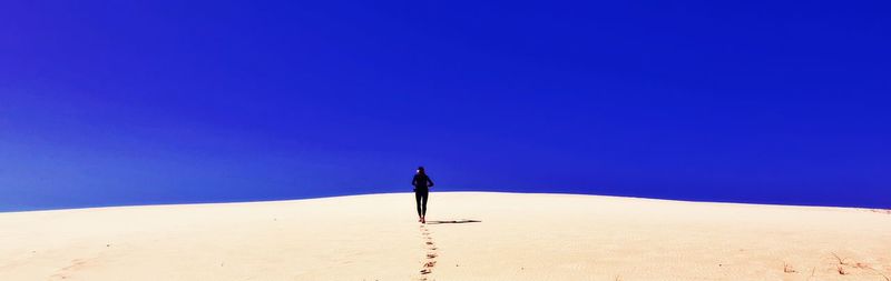 Man standing on desert against clear blue sky