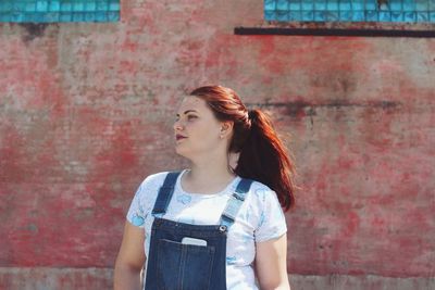 Beautiful young woman looking away against wall