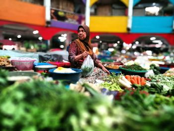 Mature owner surrounded with vegetables at supermarket